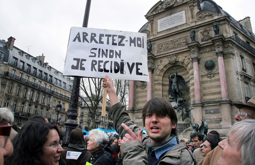 Человек, протестующий против закона, который запрещает оказывать помощь нелегальным иммигрантам, 8 апреля 2009 г., площадь Сен-Мишель в Париже, Франция. Плакат гласит: “Арестуйте меня, иначе я сделаю это снова”. Olga Besnard / Shutterstock.com