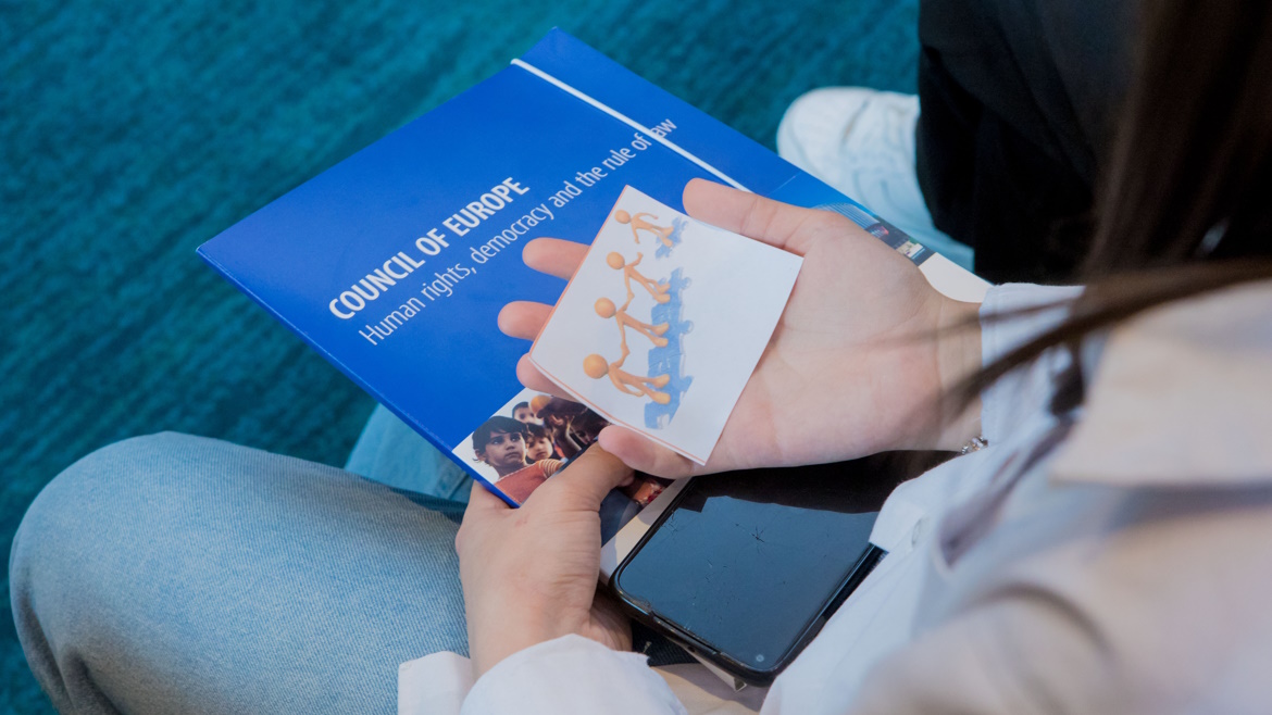 School student holding a booklet on the Council of Europe and a picture of figures holding hands